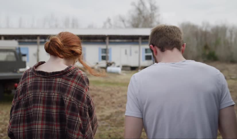 A man and woman staring at the ground walking slowly toward a home