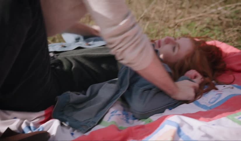 Man holds down woman on blanket on grass