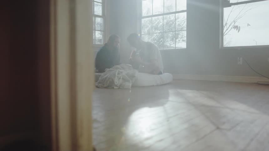 A man and woman sit on a mattress in an empty room at day time