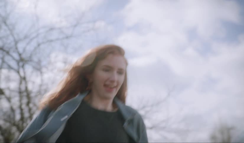 A woman in a jean jacket running and tackling someone out in a field