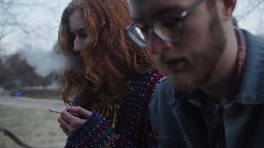A woman is smoking next to a man in glasses