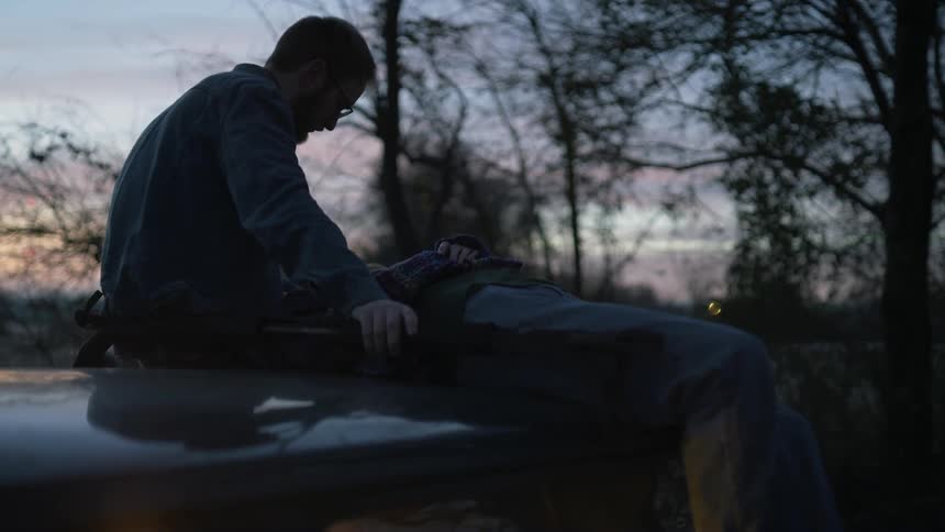 A woman laying on top of a man outdoors at dusk