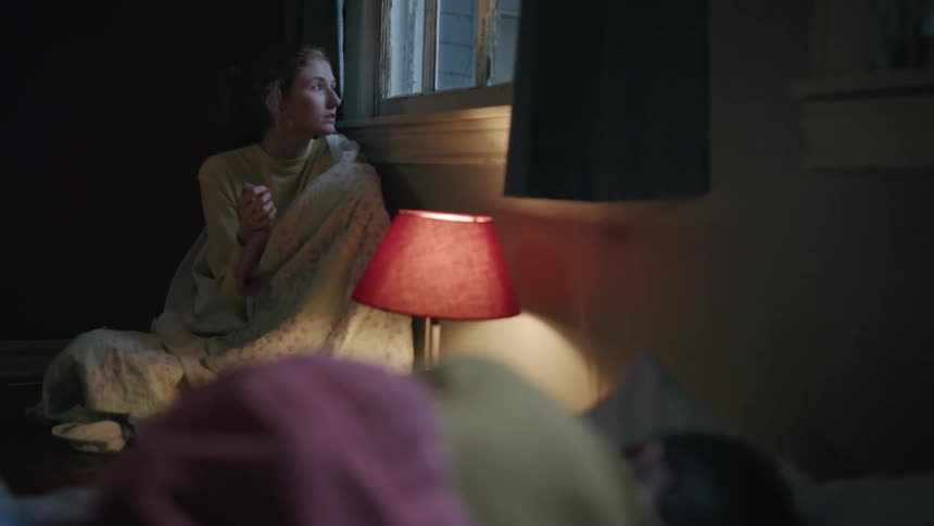 A woman covered in a blanket is smoking next to a window