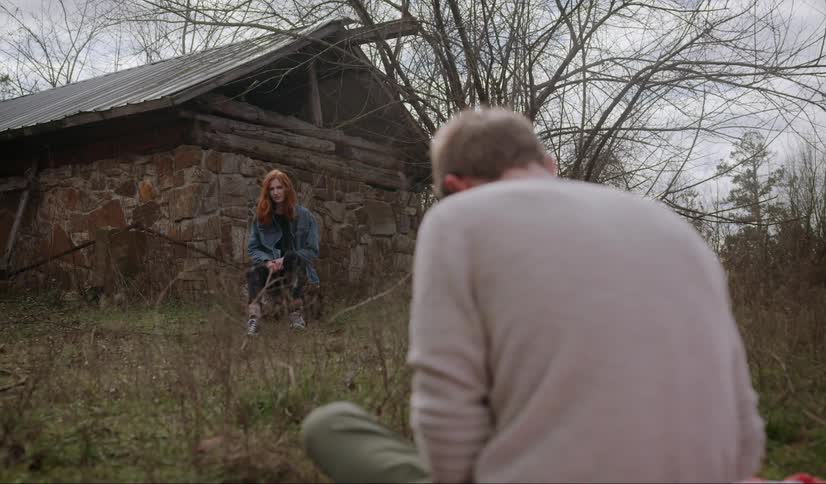 A man sitting in a field looking at a woman next to a house