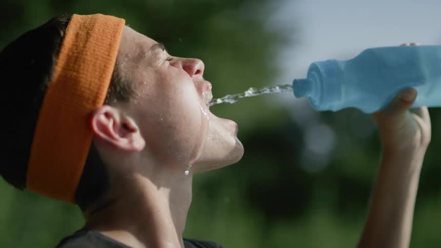 A young man squirts water to his mouth