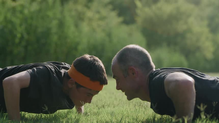A man and a boy do pushups and touch hands each time they come up from one