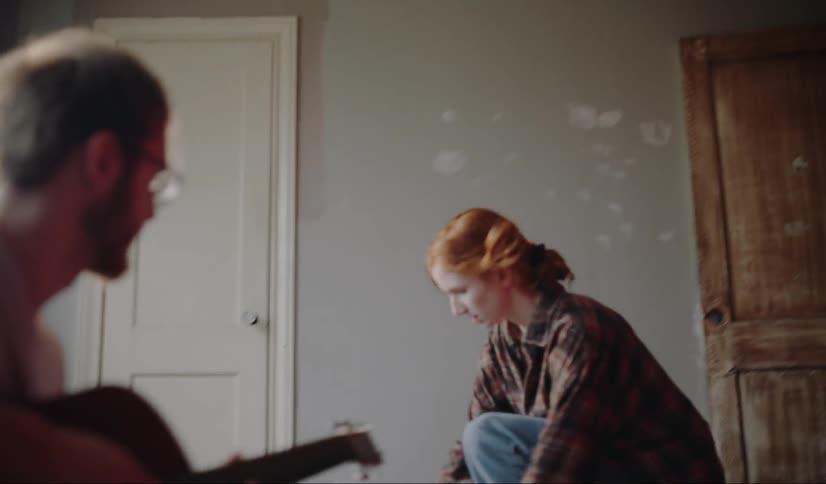 A man playing a guitar while a woman runs into the room