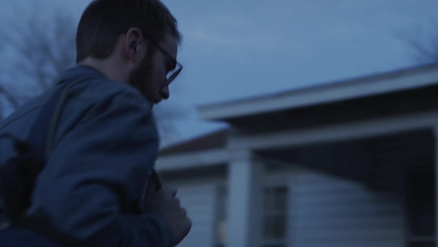 A man with a backpack walks up porch stairs to a house
