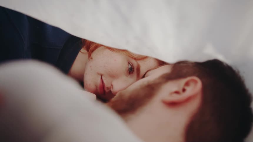 A woman and man lay beside each other under a sheet