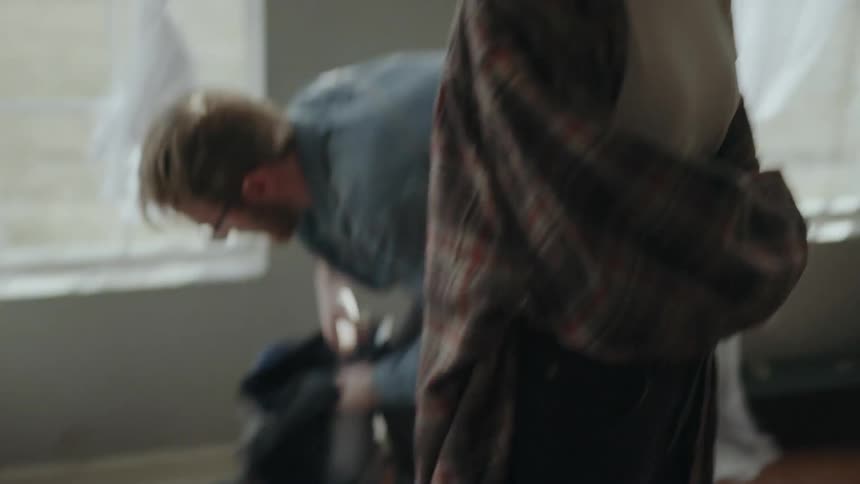 A man talking to a woman and then packing up clothes in a bag