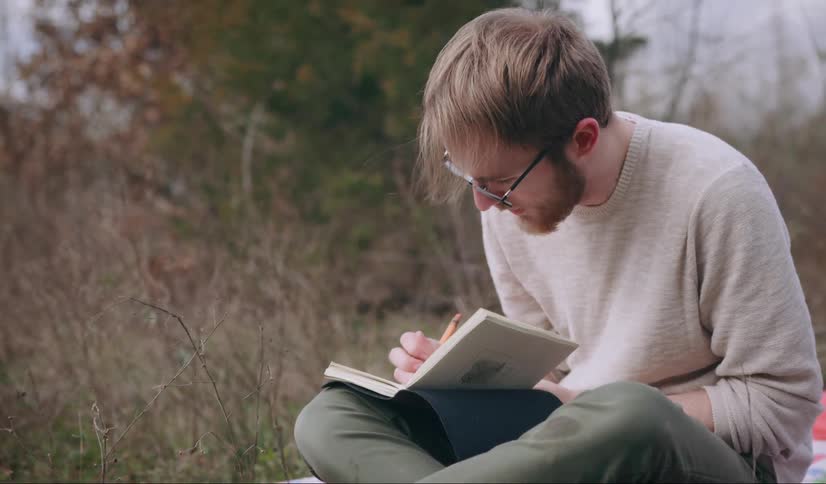 A man sitting in a field sketching in a book