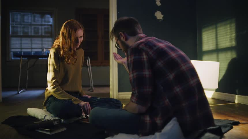 A man and a woman sit on the floor playing a board game in the dark