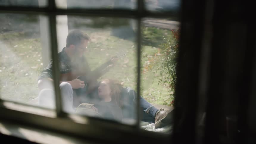 A man sits outside on a porch playing a guitar
