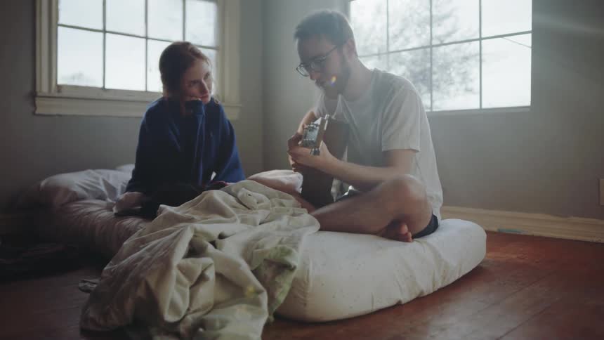 A woman sitting beside a man playing guitar