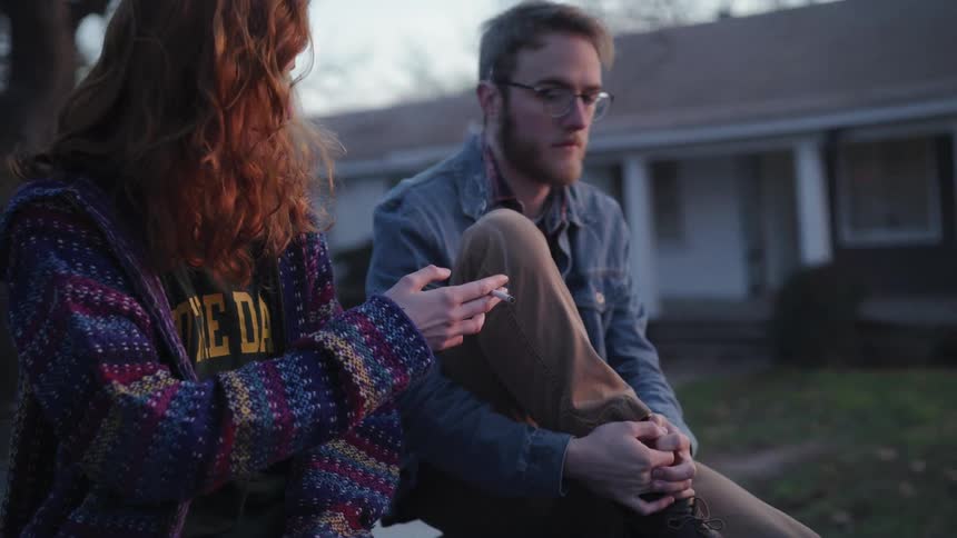 A woman takes a drag off of a cigarette then hands the cigarette to the man next to her