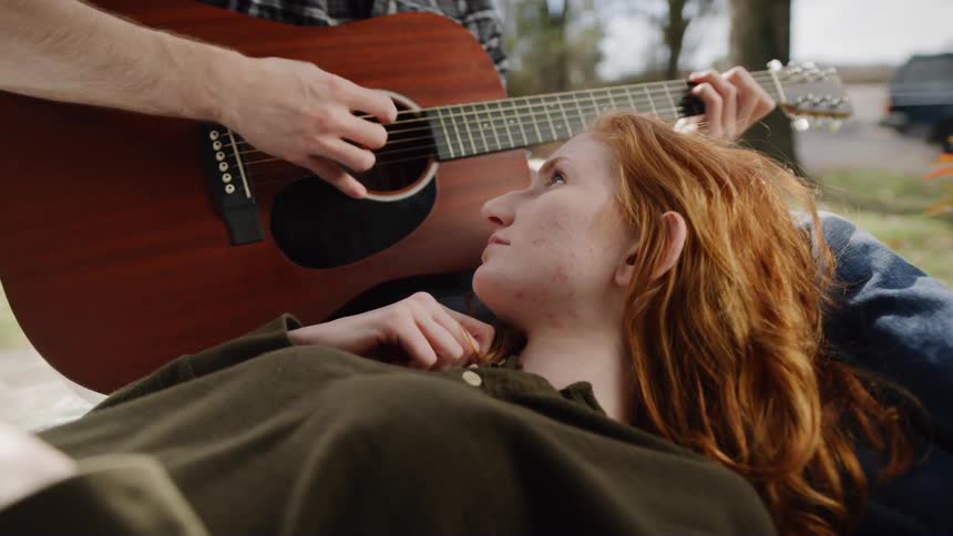 Woman laying with her head in the lap of a man playing the guitar