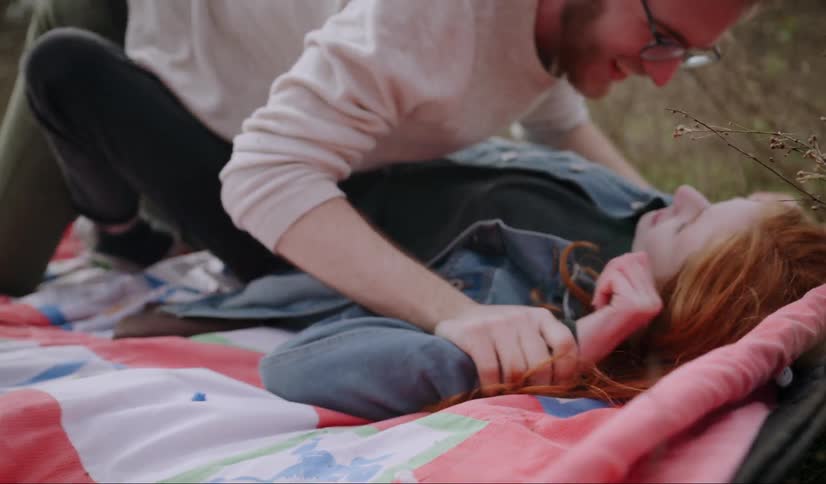 A man and woman are rolling on a blanket outdoors