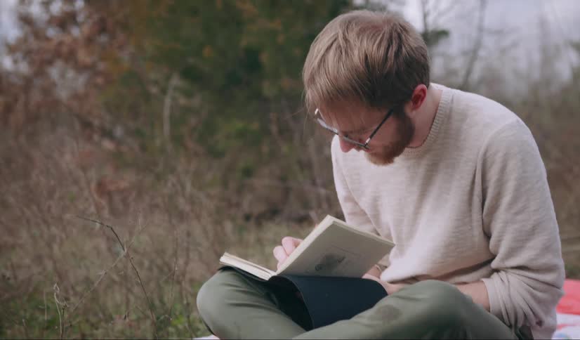 A man sits in the countryside writing in a book