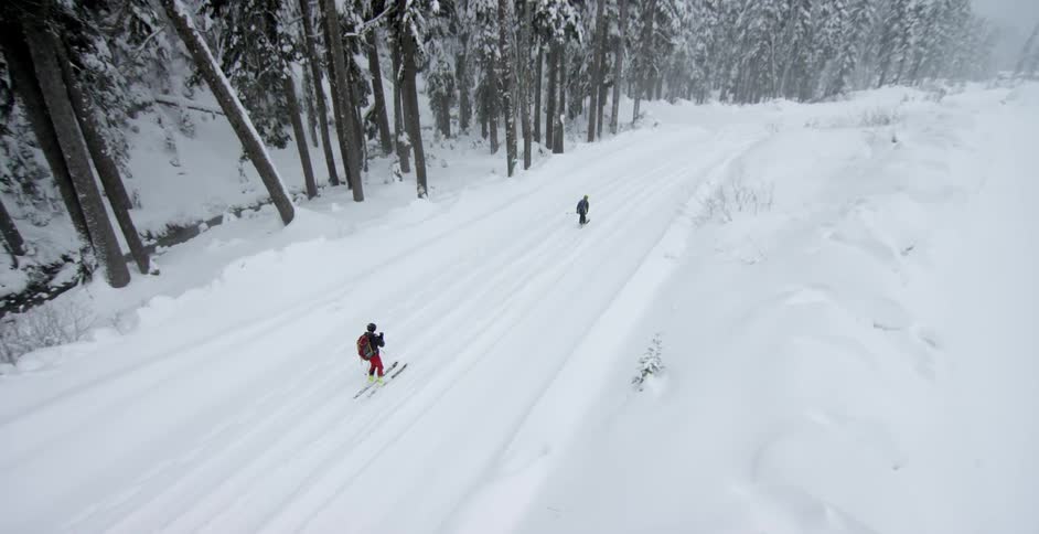 Two people ski down a snowy hill
