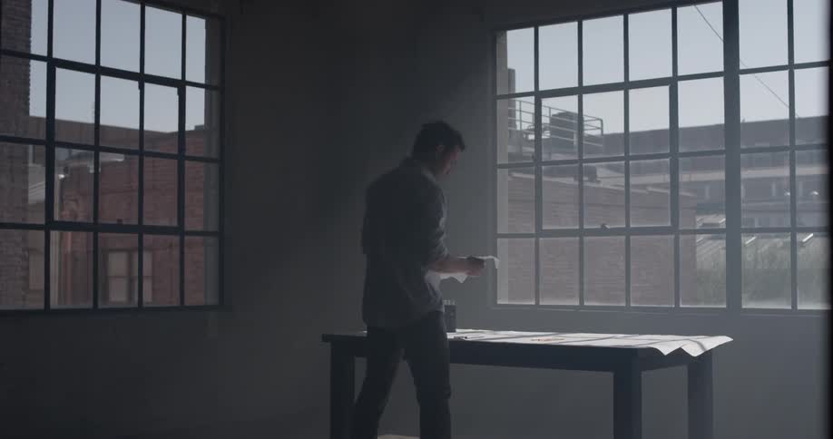 A man walks to a table and picks up a paper and then a pencil