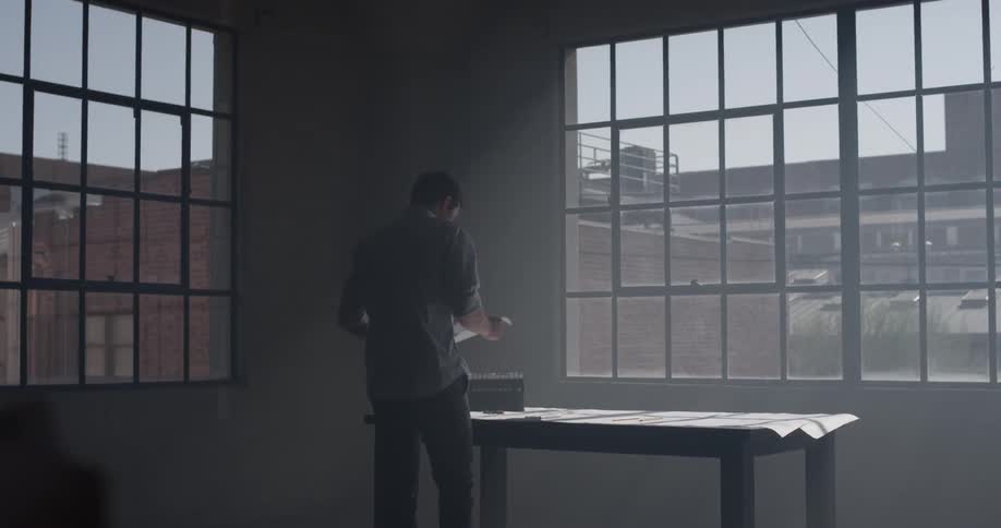 A man walking into a room and grabbing some paper on a desk
