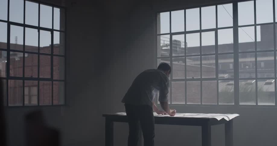 A man hovers over a table in a naturally lit room writing on paper