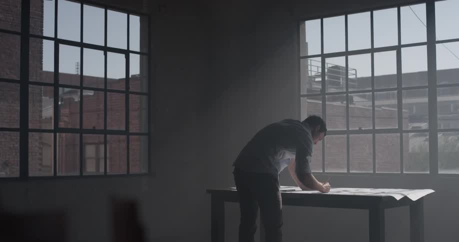 A man sketching on a piece of paper in front of an open window