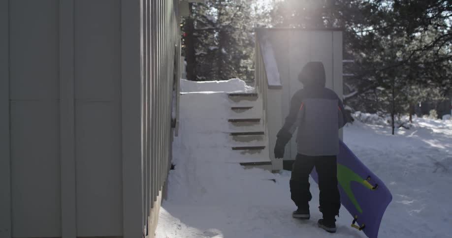 Person walks in the snow toward a building with a body board
