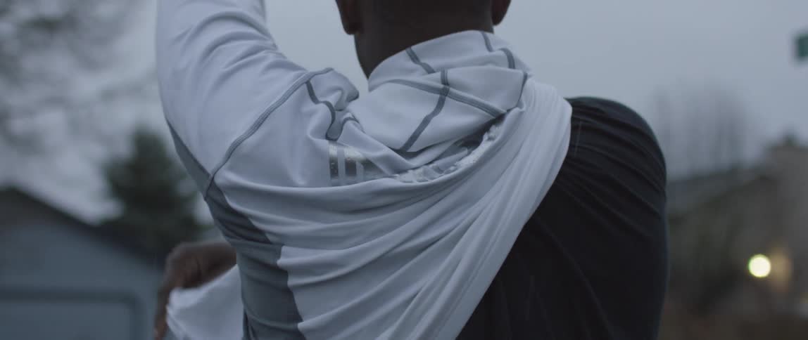 A man is walking through a neighborhood and taking off his jacket