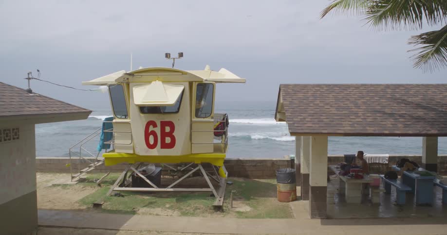 Two men sitting in a covered picnic area next to the lifeguard tower on the beach