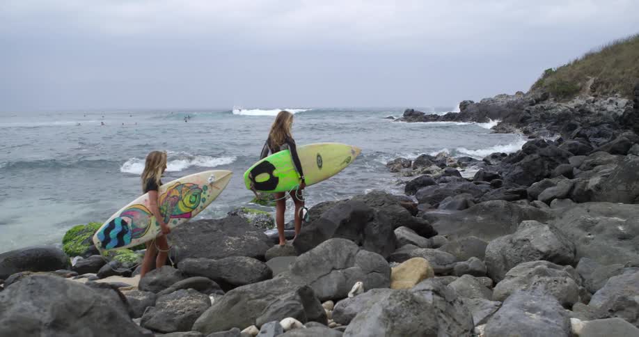 Surfers are walking on the rocky beach