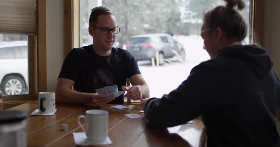 A man and woman playing cards while sitting near a big window