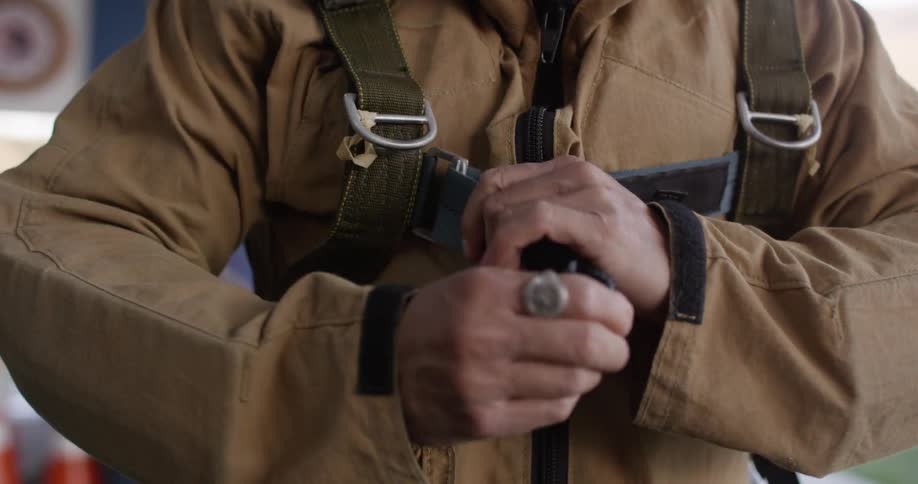 A man in a flight suit adjusts the straps of his parachute