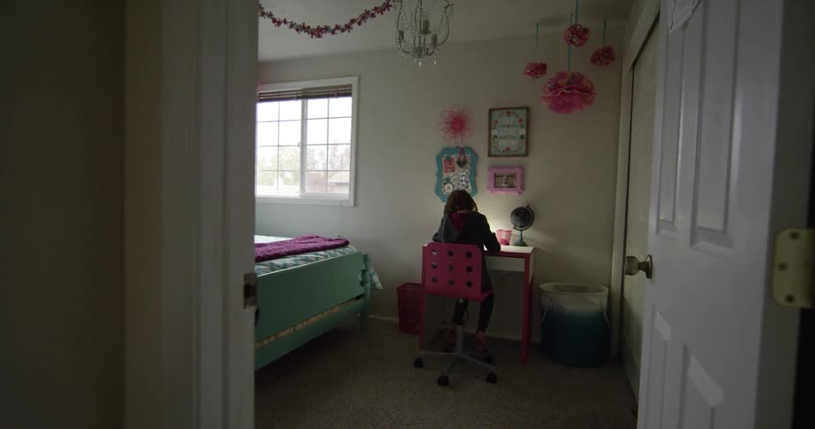 A girl sits at her desk in her bedroom
