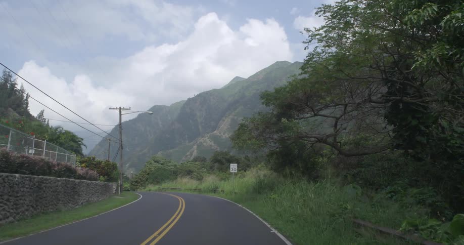 Driving down a road with hills, trees and brush along side
