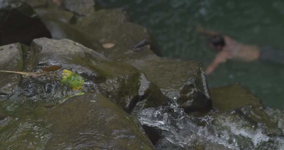 Water flows down a rocky ledge as a man swims below