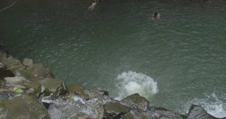 Man jumps from the top of a small waterfall into a river