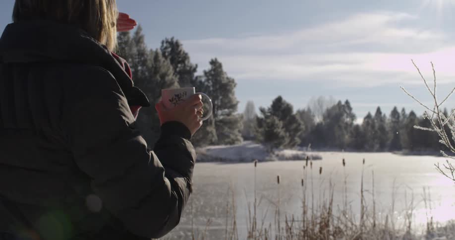 A woman drinking from a mug and overlooking a snowy area