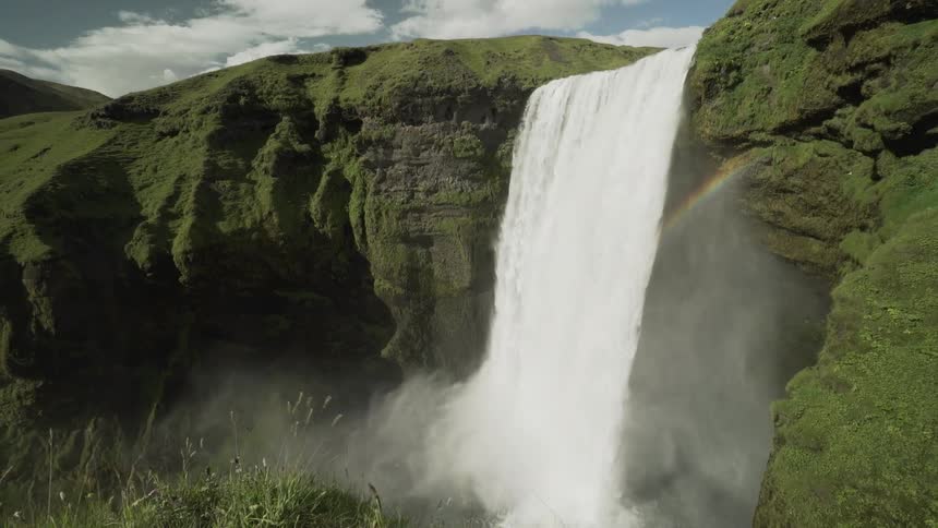 A waterfall cascades down a green rocky ledge