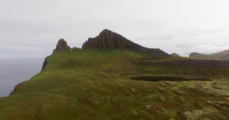A mountain top covered with green grass and a cloudy sky