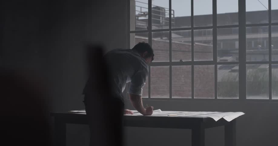 Man drawing on a large paper lined table in front of a window