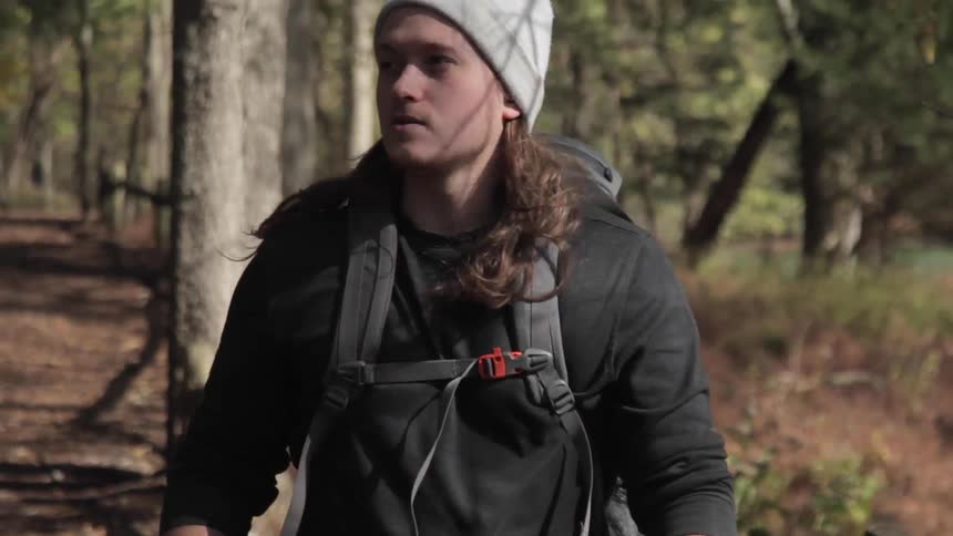 A young man wearing a large backpack and using walking sticks as he hikes through the woods