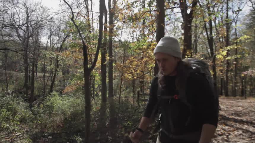 Male hiker with walking sticks and backpack walks along a wooded trail