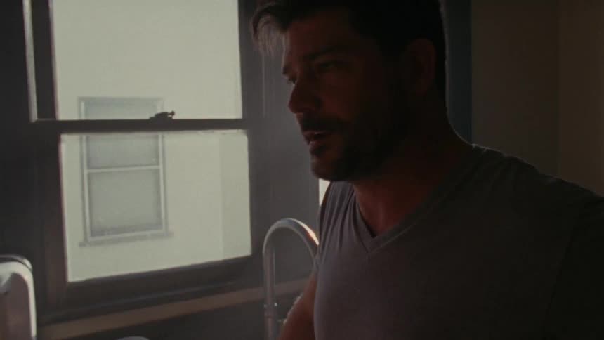 Man in a gray t-shirt talking with someone indoors