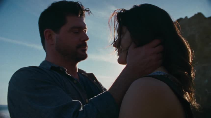 A man and woman kiss on the beach