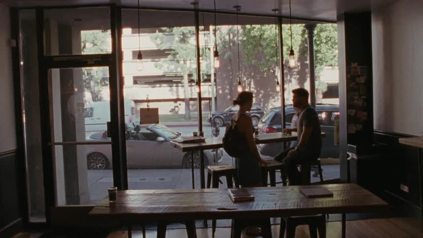 Woman entering a cafe and greeting a man sitting at the window counter