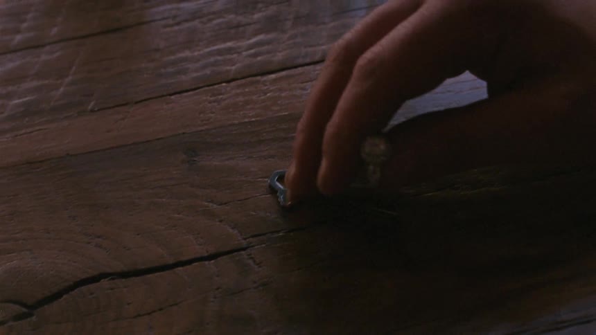 A woman sliding a ring and keys over a wood surface before a man picks up the ring and slides the key over
