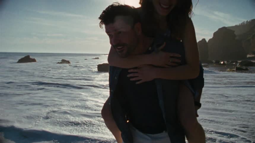 A woman rides on a mans back on the beach