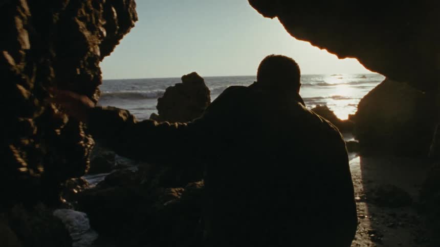 Bearded man walking on the beach with tall rocks all around