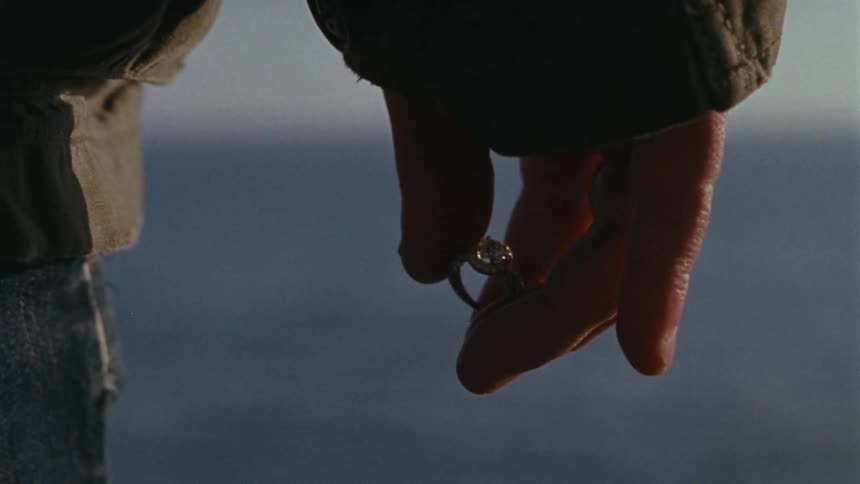 A man fidgeting with a diamond ring as he overlooks an ocean